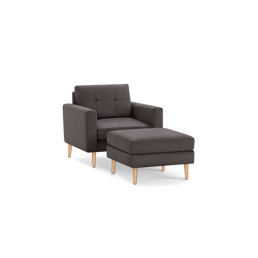 Modern dark gray fabric armchair with matching ottoman, both featuring wooden tapered legs and tufted backrest.
