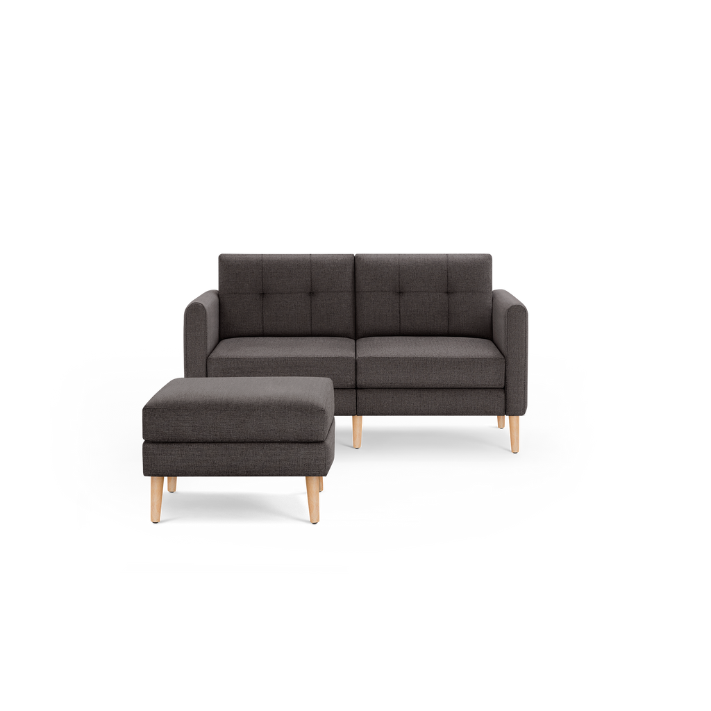 Dark gray two-seater sofa with tufted backrest and matching ottoman, both featuring light wooden legs.