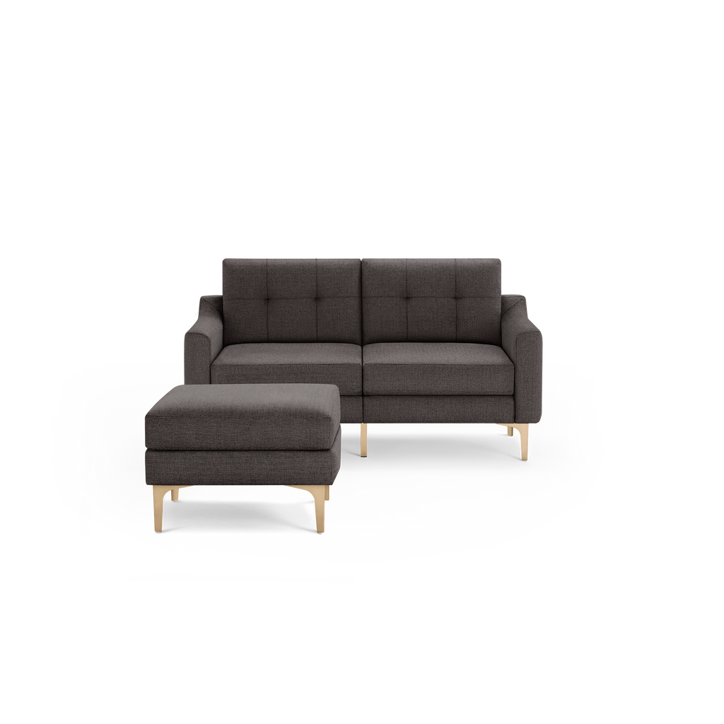 Dark gray upholstered loveseat with tufted back, slim gold metal legs, and matching square ottoman on black background.