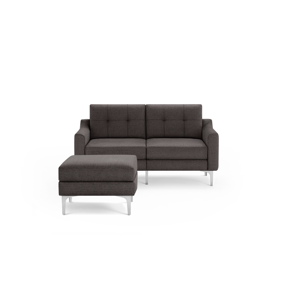 Modern dark gray fabric loveseat with tufted backrest and matching ottoman, both supported by sleek metal legs.