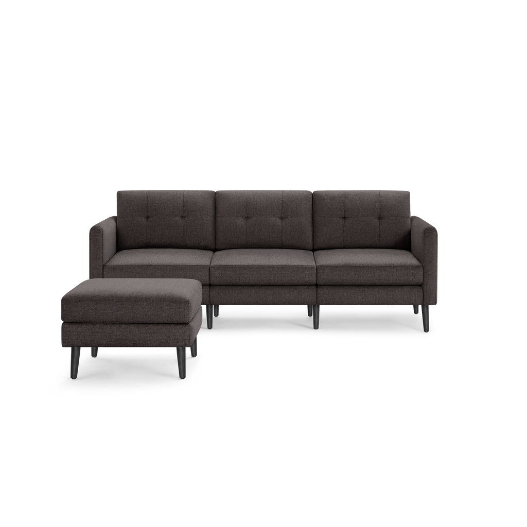 Dark gray fabric sectional sofa with tufted back cushions, three seat cushions, square arms, and matching ottoman on black wooden legs.