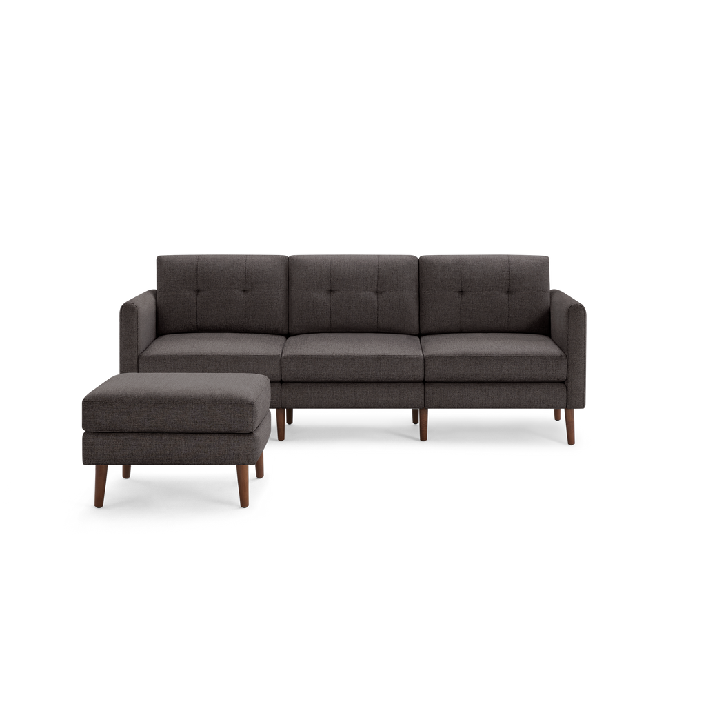 Dark gray fabric sectional sofa with tufted back cushions, wooden legs, and matching ottoman on the left side.