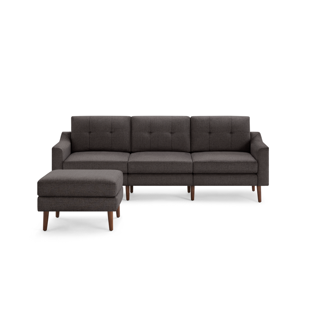 Dark gray fabric three-seater sofa with left-side matching ottoman, button-tufted back cushions, and wooden tapered legs.