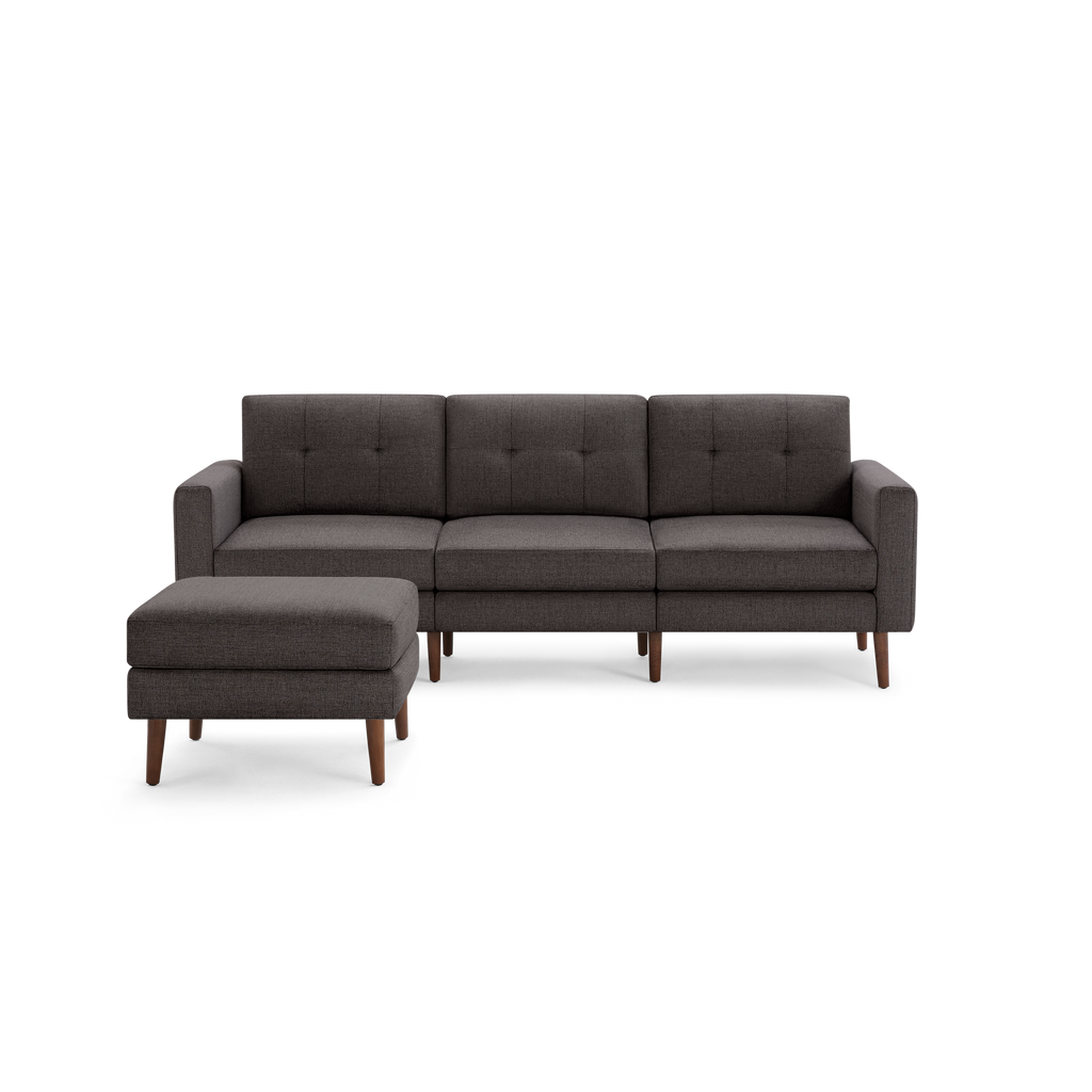 Modern dark gray fabric sectional sofa with tufted cushions and wooden legs, featuring a matching cushioned ottoman on the left side.