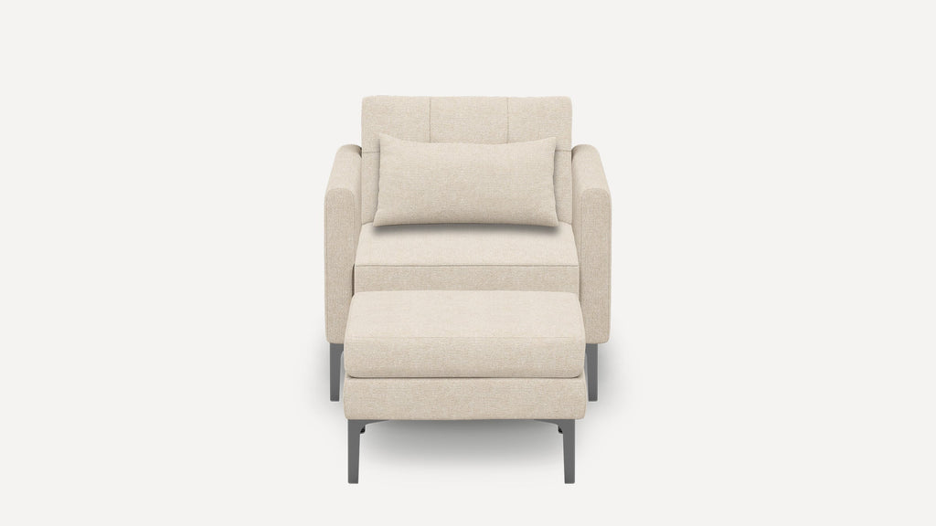Beige upholstered armchair with matching rectangular pillow and ottoman, featuring slim dark metal legs, shown on white background.