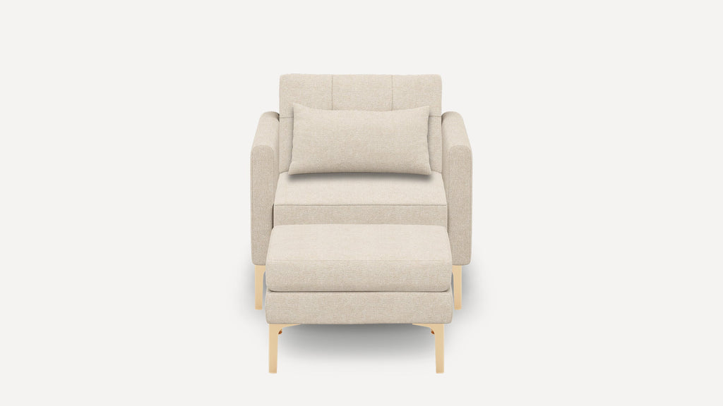Front view of a modern beige upholstered armchair with matching ottoman and rectangular lumbar pillow, featuring light wooden legs.