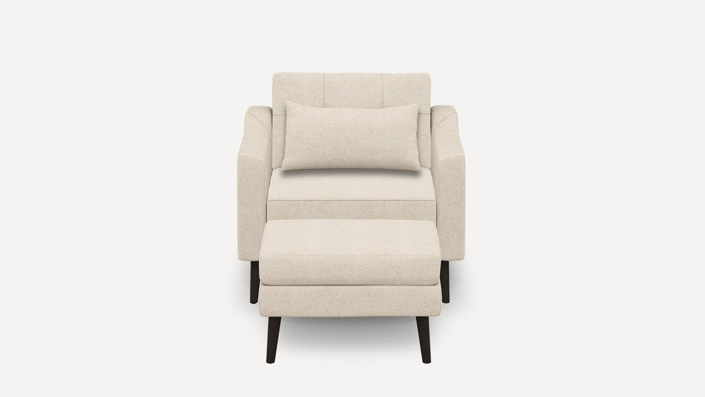 Beige upholstered armchair with matching rectangular lumbar pillow and separate cushioned ottoman, supported by dark wooden legs.