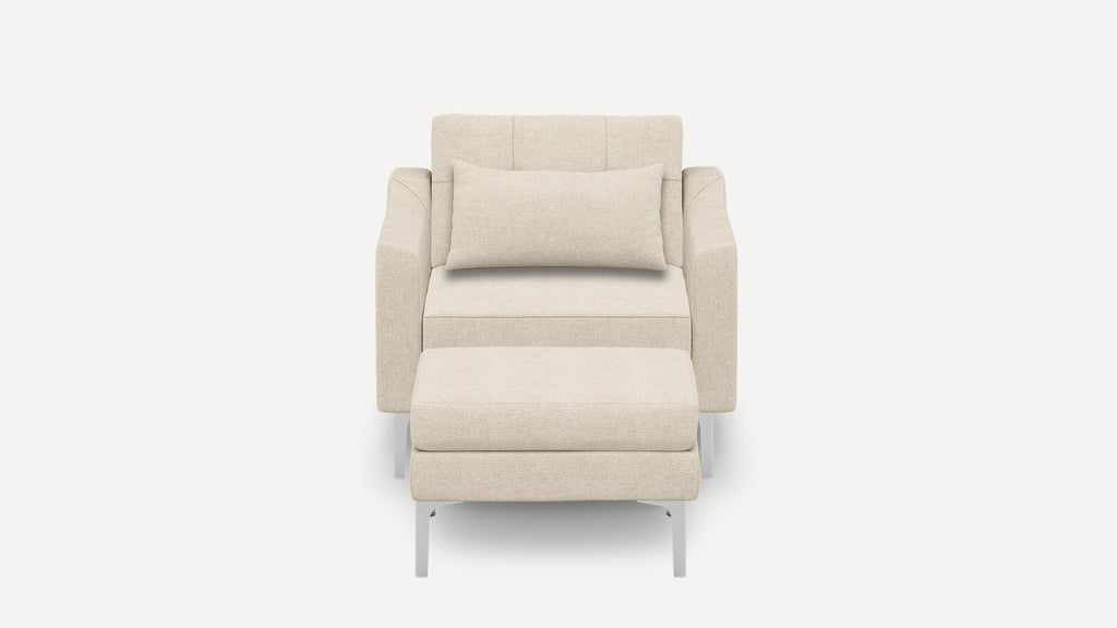 Front view of a modern beige fabric armchair with matching cushioned ottoman and rectangular lumbar pillow, supported by silver metal legs.