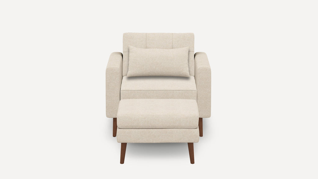 Beige upholstered armchair with matching ottoman and rectangular lumbar pillow, featuring wooden legs and clean, modern design.