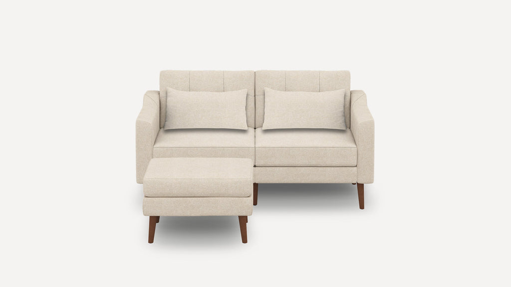 Beige two-seater sofa with two matching rectangular cushions and a separate beige ottoman, all with wooden legs.