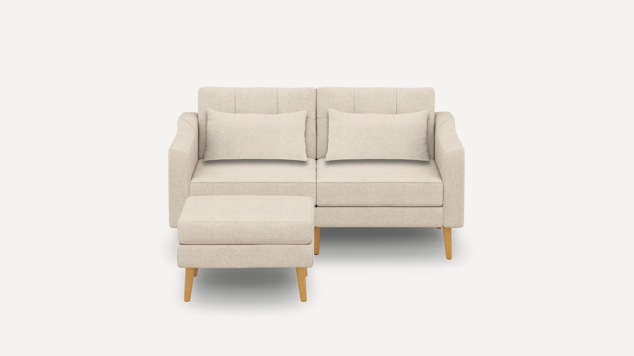Beige fabric loveseat sofa with two matching pillows and a separate ottoman, featuring wooden legs and a modern design.