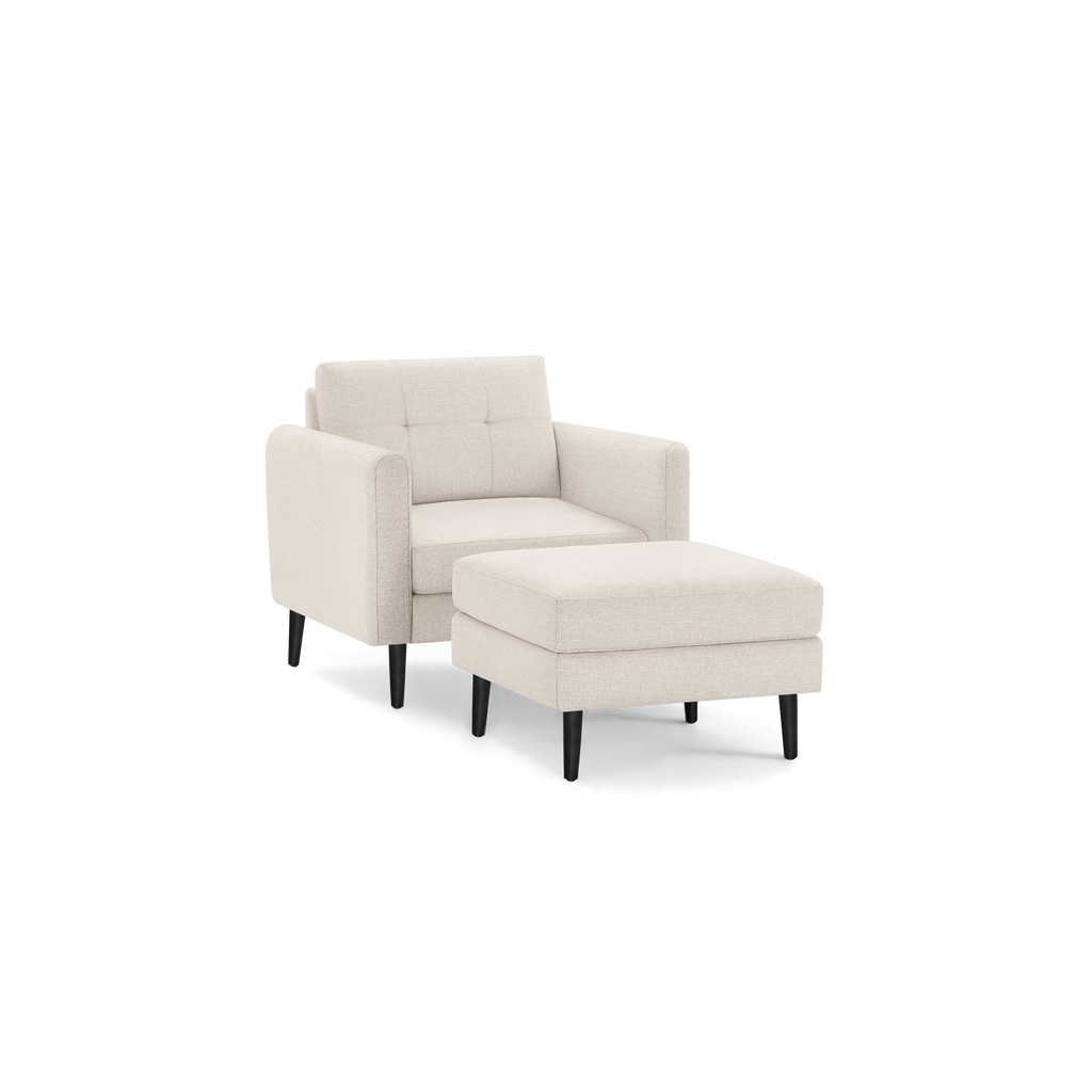 Beige fabric armchair with tufted backrest and matching ottoman, both supported by black wooden legs.