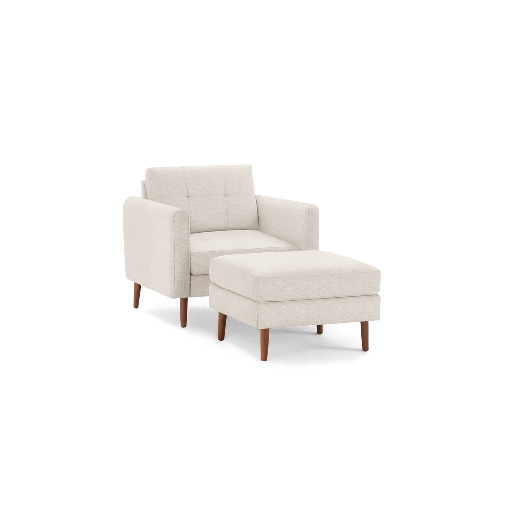 Beige fabric armchair with matching cushioned ottoman, featuring wooden legs and tufted backrest, isolated on black background.