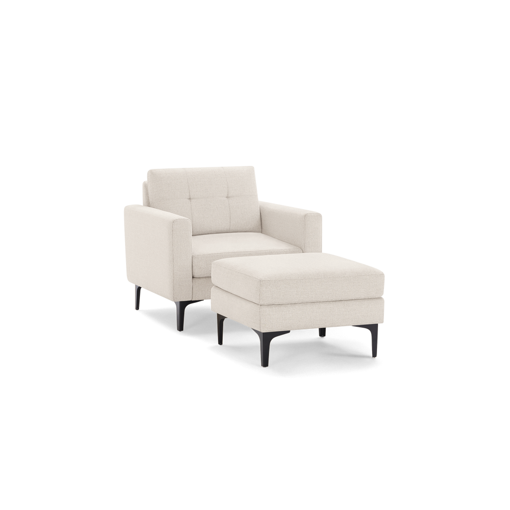 Beige fabric armchair with tufted backrest and matching cushioned ottoman, supported by slim black legs.