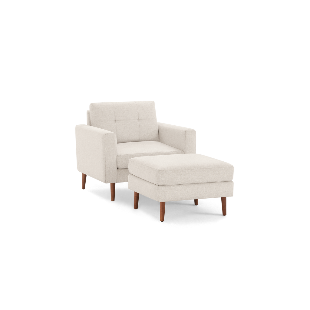 Beige upholstered armchair with tufted backrest and matching ottoman, both featuring wooden legs in a mid-century modern style.