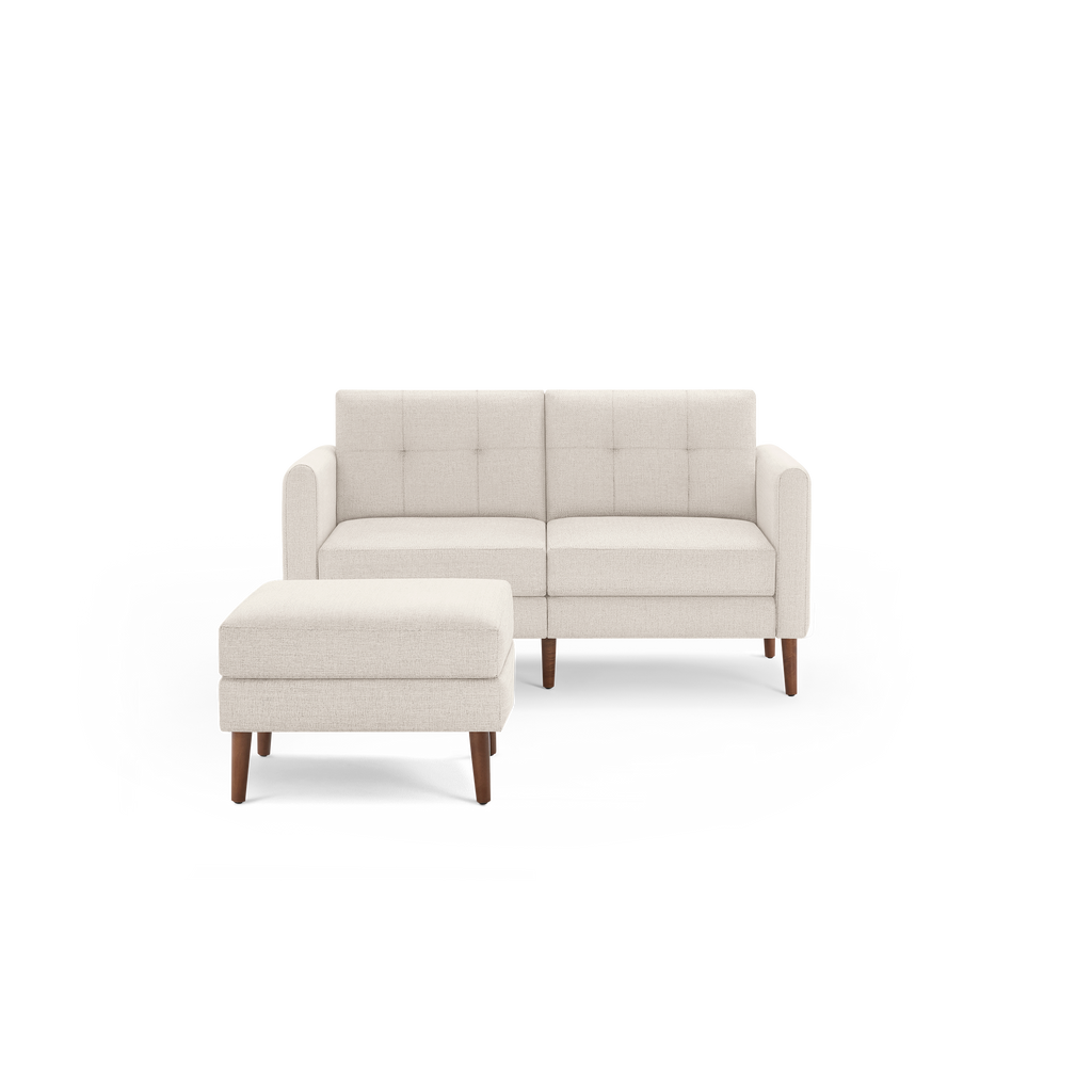 Beige fabric two-seater sofa with tufted backrest, matching ottoman, and wooden legs.
