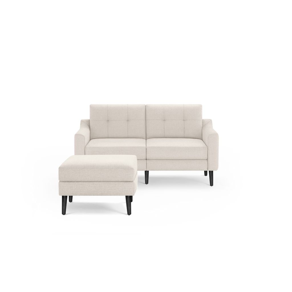 Beige two-seater sofa with button-tufted backrest and matching ottoman, both featuring black wooden legs.