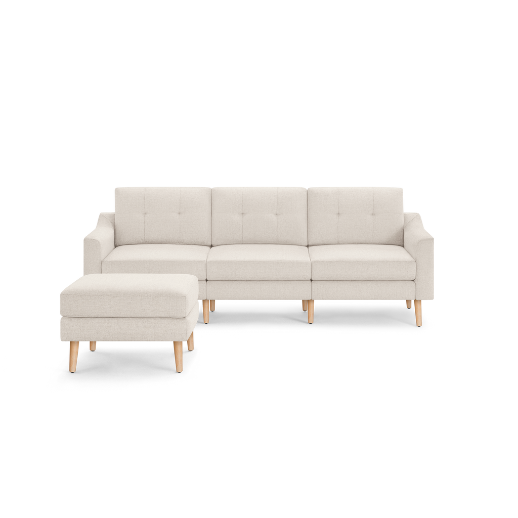 Light beige fabric sectional sofa with tufted back cushions and matching ottoman, supported by light wooden legs.