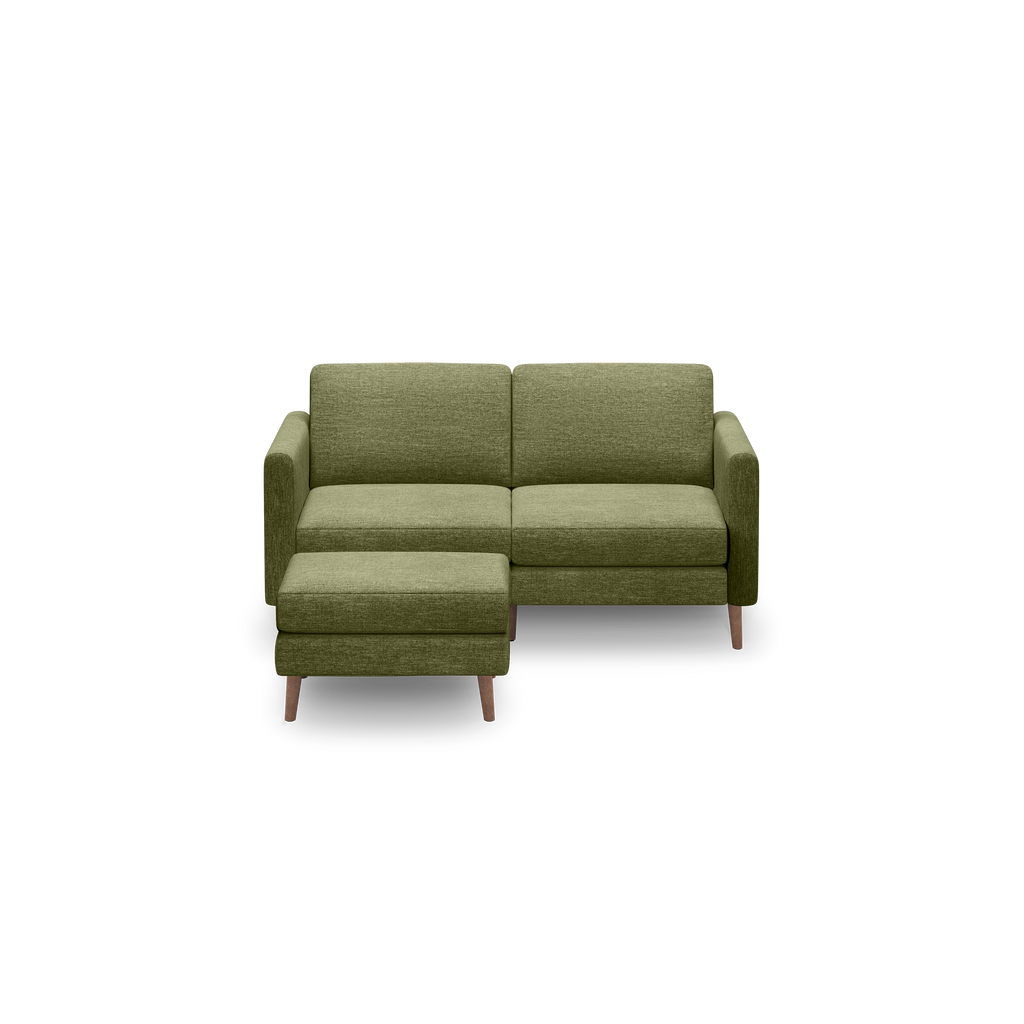 Olive green upholstered two-seater sofa with matching ottoman, square armrests, and wooden legs, isolated on black background.