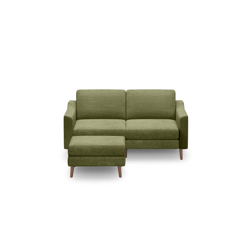 Green fabric two-seater sofa with wooden legs and a matching upholstered ottoman on a black background.
