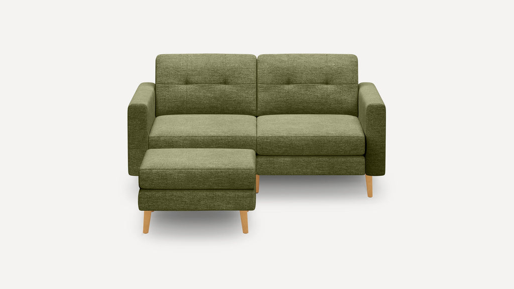 Modern olive green fabric loveseat with tufted back cushions, straight arms, matching ottoman, and light wooden legs on white background.