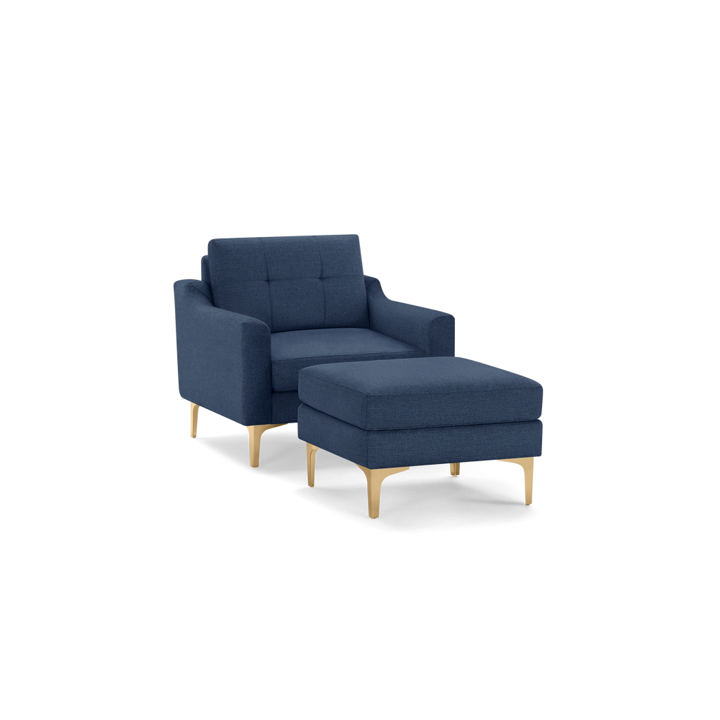 Modern navy blue upholstered armchair with matching ottoman, featuring tufted cushions and light wooden legs.