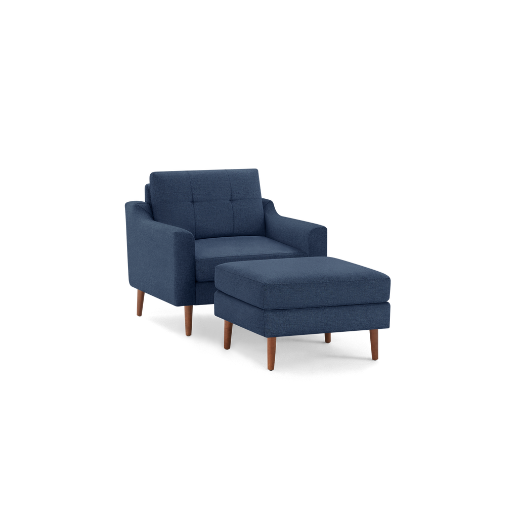 Modern navy blue upholstered armchair with tufted backrest and matching cushioned ottoman, both featuring wooden legs.