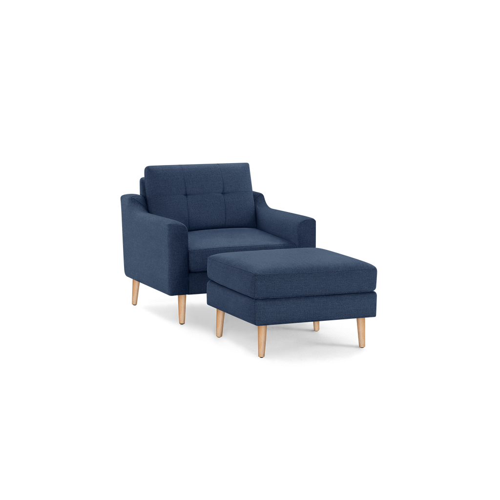 Modern navy blue fabric armchair with matching cushioned ottoman, both featuring light wooden legs.