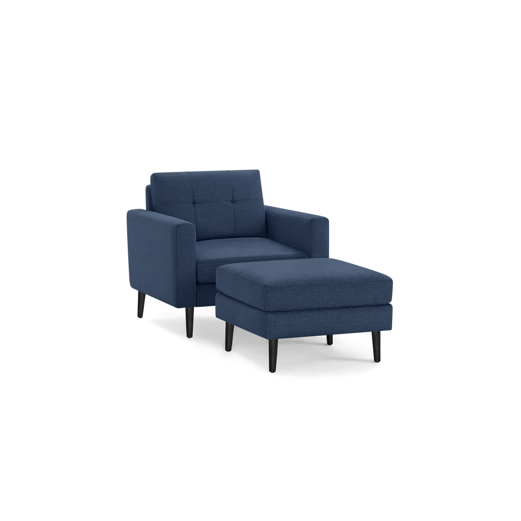 Modern navy blue upholstered armchair with matching cushioned ottoman, featuring black tapered wooden legs and tufted backrest.