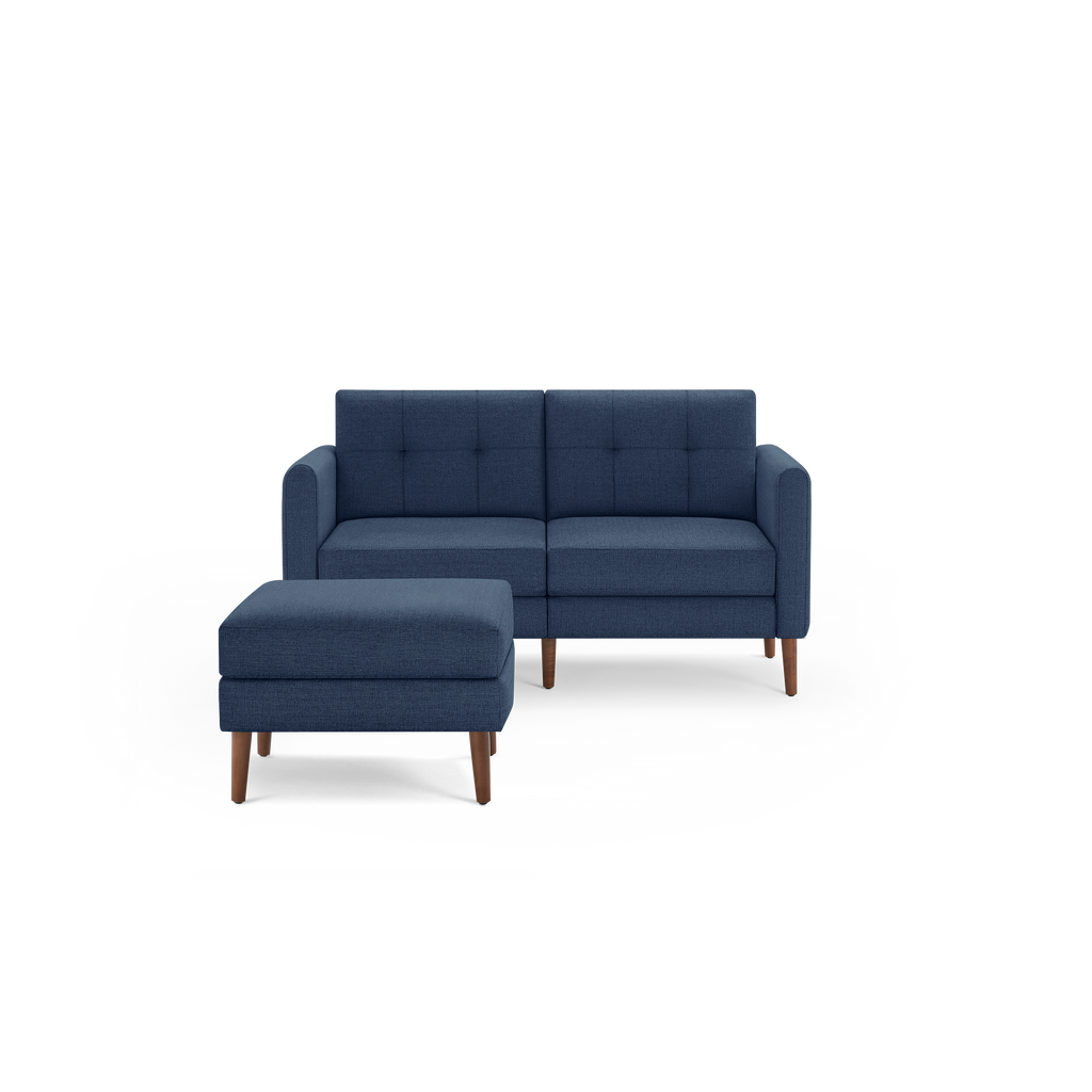 Modern two-seater navy blue fabric sofa with tufted back cushions and matching ottoman, both featuring wooden legs.