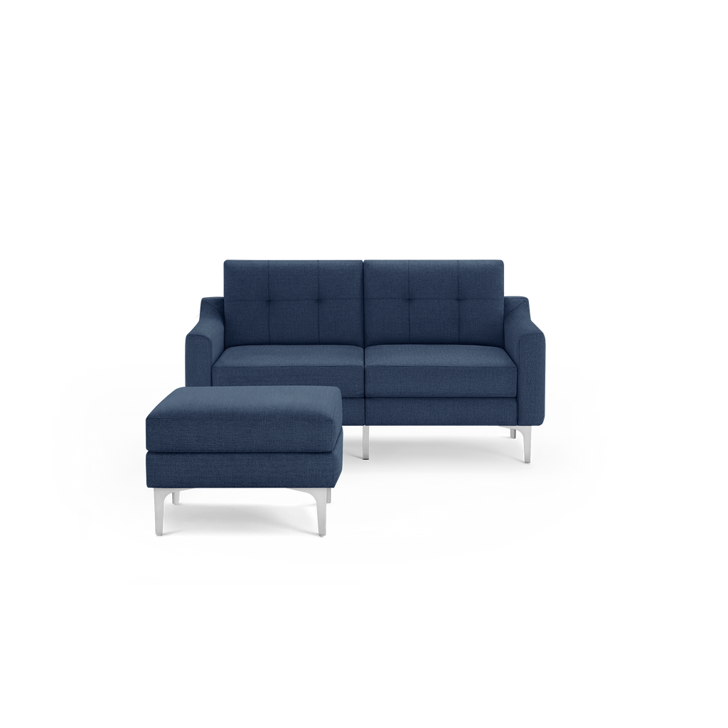 Modern navy blue fabric loveseat with tufted cushions and matching ottoman, supported by sleek silver metal legs.