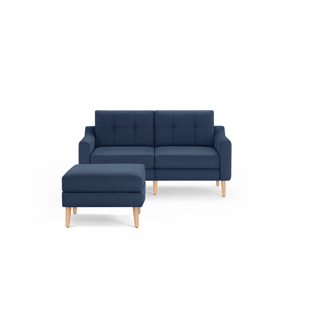 Modern navy blue fabric loveseat with tufted backrest and matching ottoman, both supported by light wooden legs.
