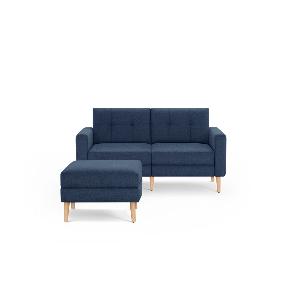 Mid-century modern navy blue fabric loveseat sofa with tufted back cushions and matching ottoman, both with light wooden legs.
