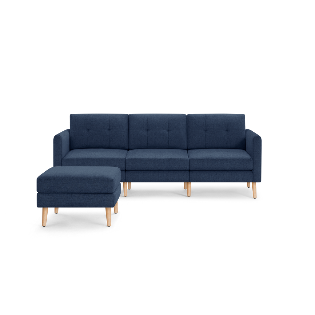 Modern navy blue fabric sectional sofa with a matching ottoman, featuring wooden legs and button-tufted back cushions.