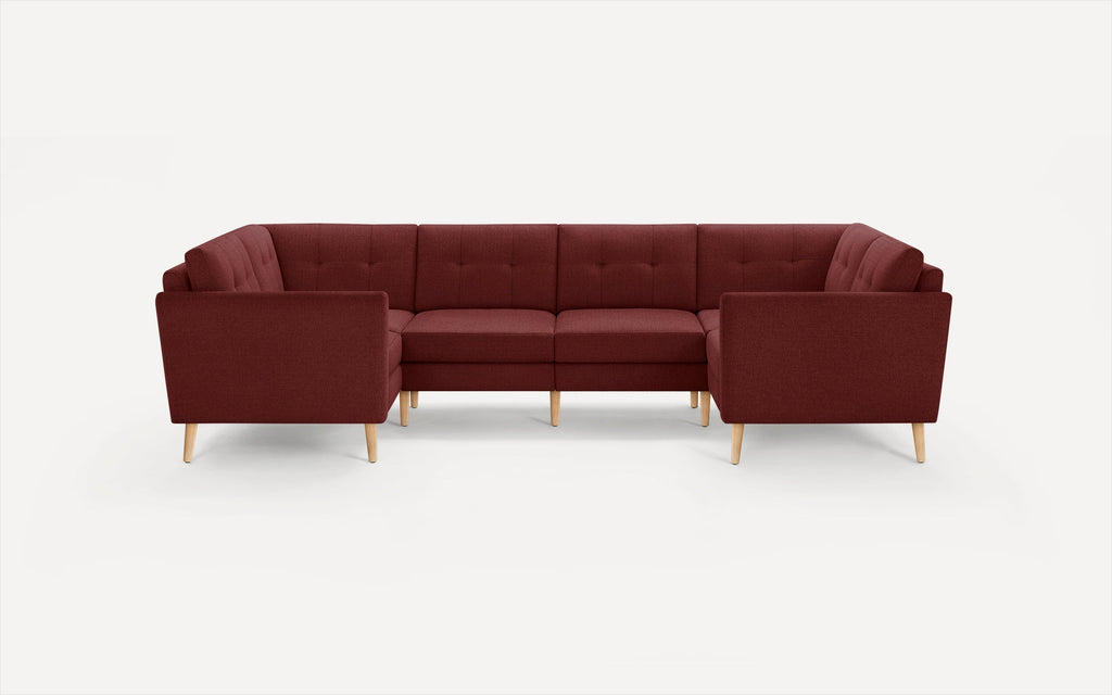Modern sectional sofa in deep burgundy fabric with tufted back cushions and light wooden tapered legs, arranged in a U-shape.