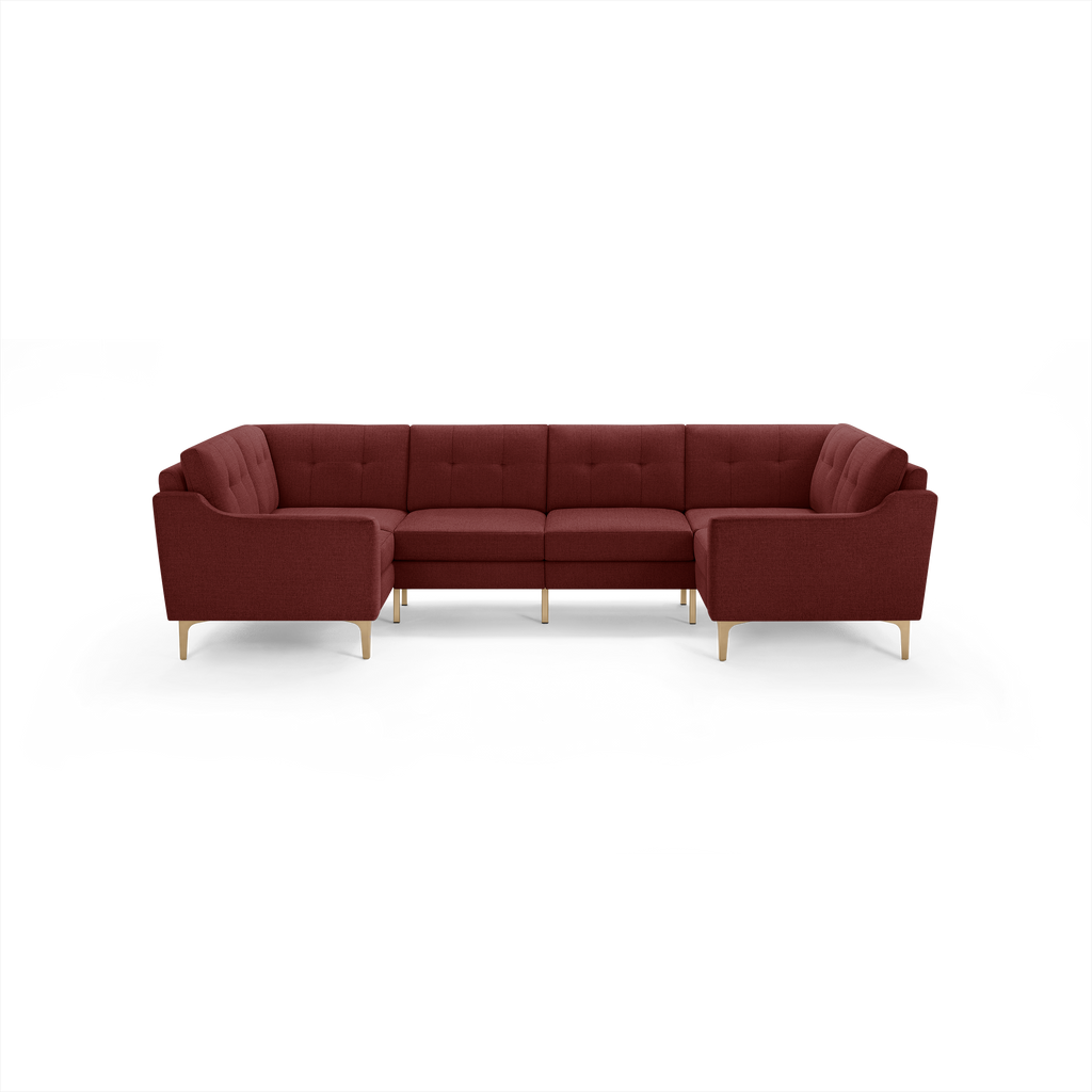 Large L-shaped sectional sofa in deep burgundy fabric with tufted back cushions and light wooden legs.