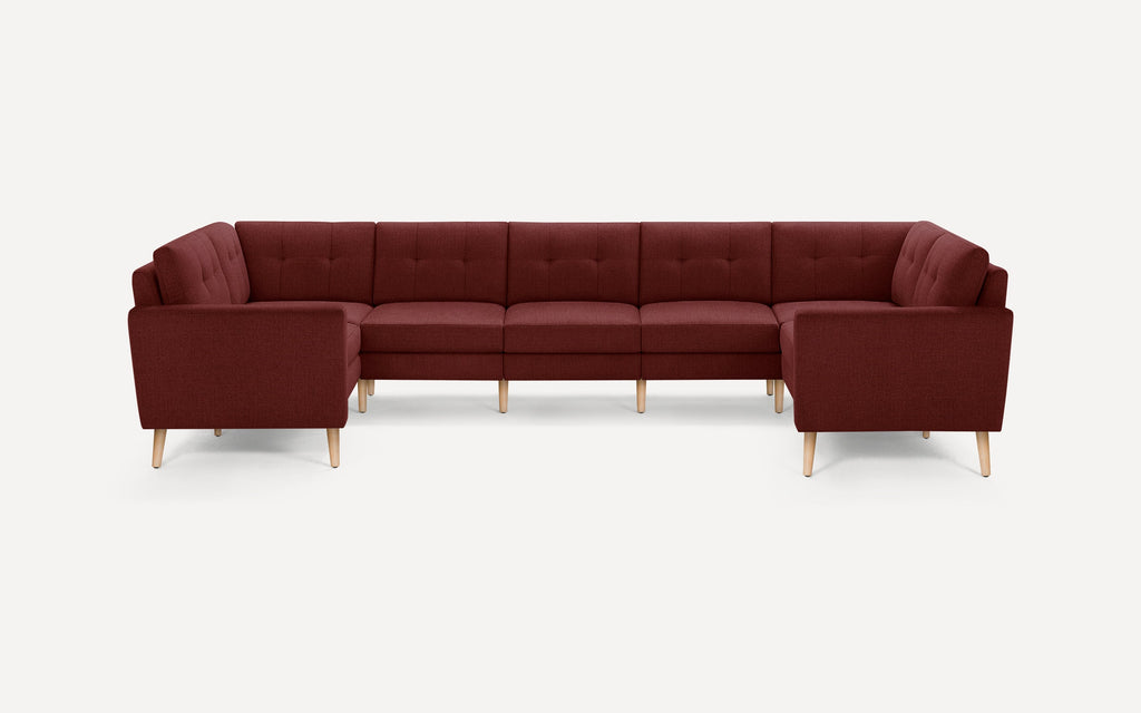 Large sectional sofa in a deep burgundy fabric with tufted back cushions and light wooden legs, designed for modern living rooms.
