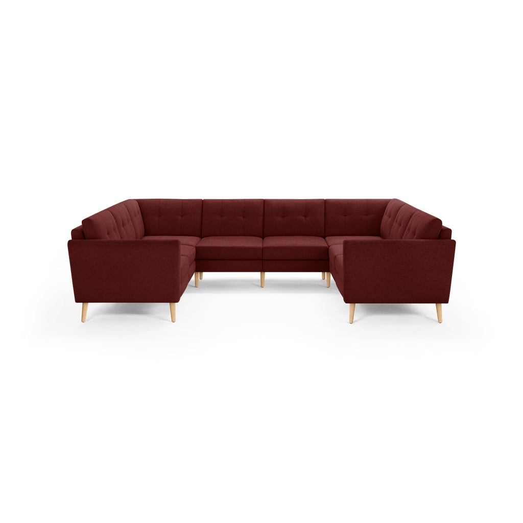 Large U-shaped sectional sofa in dark red fabric with tufted back cushions and light wooden legs.