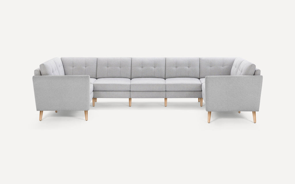 Light gray fabric U-shaped sectional sofa with tufted back cushions and wooden tapered legs on a white background.