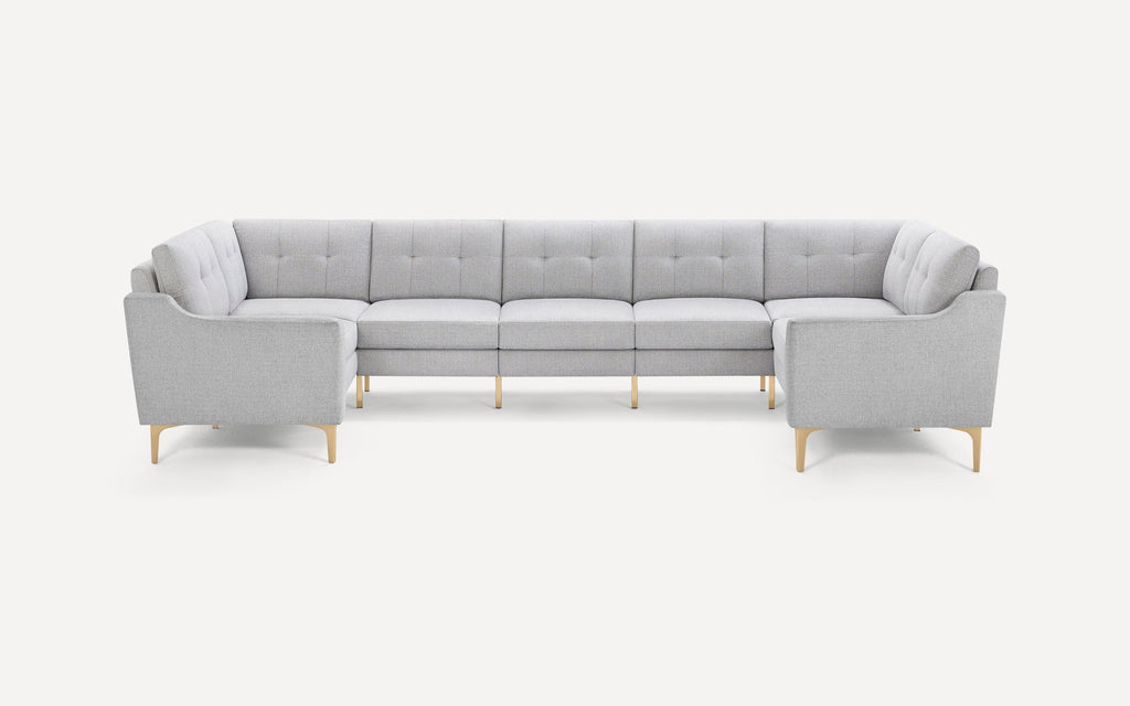 Light gray fabric upholstered sectional sofa with tufted cushions and light wooden legs, arranged in a spacious U-shape design.