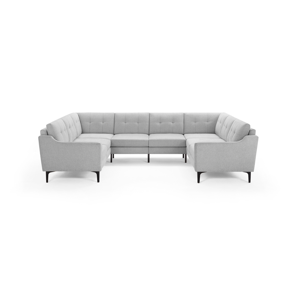 Light gray modern U-shaped sectional sofa with tufted back cushions and slim black legs on black background.