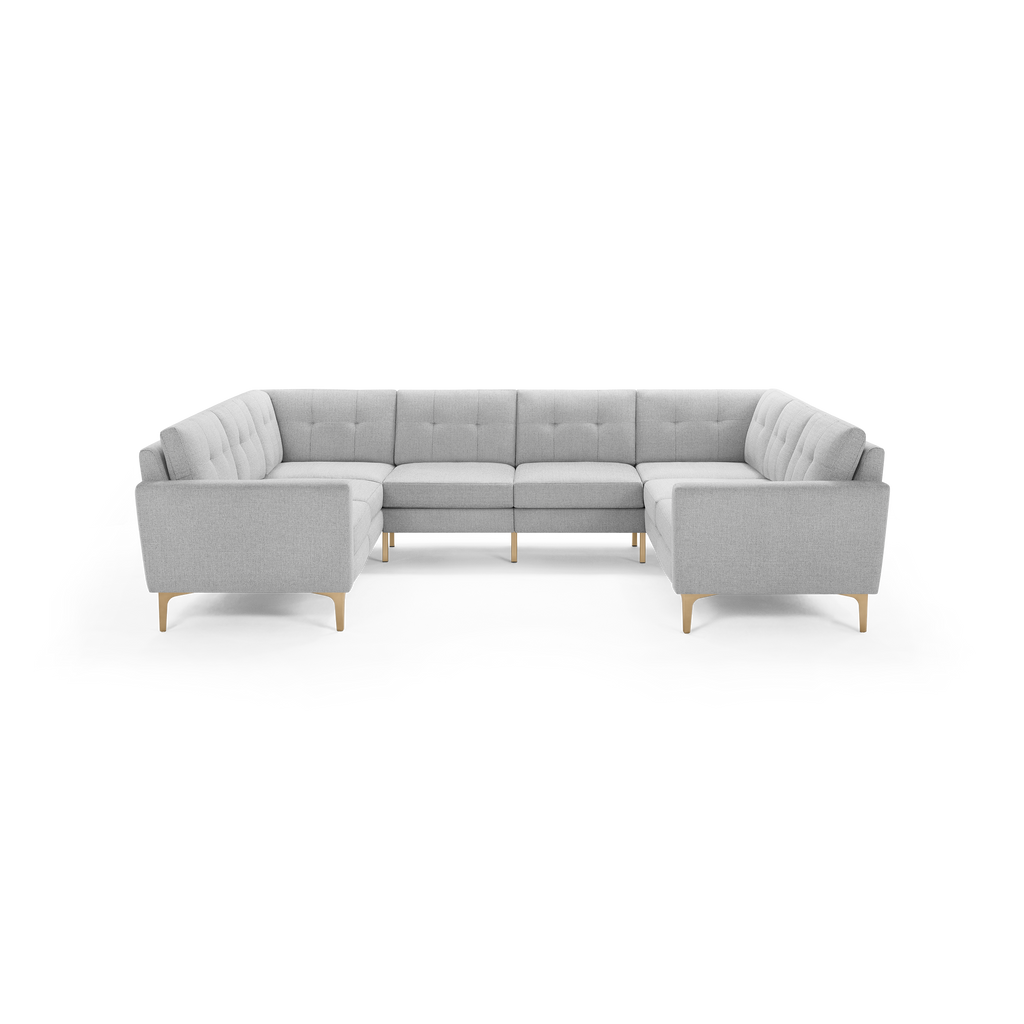 Light gray upholstered U-shaped sectional sofa with tufted back cushions and wooden legs, modern mid-century design.