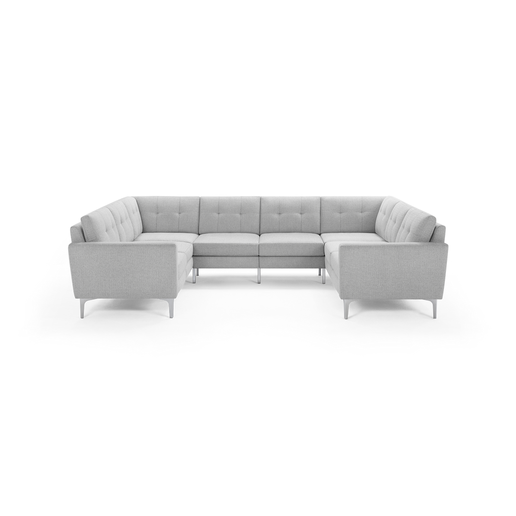 Light gray upholstered fabric U-shaped sectional sofa with tufted back cushions and slim metal legs on black background.