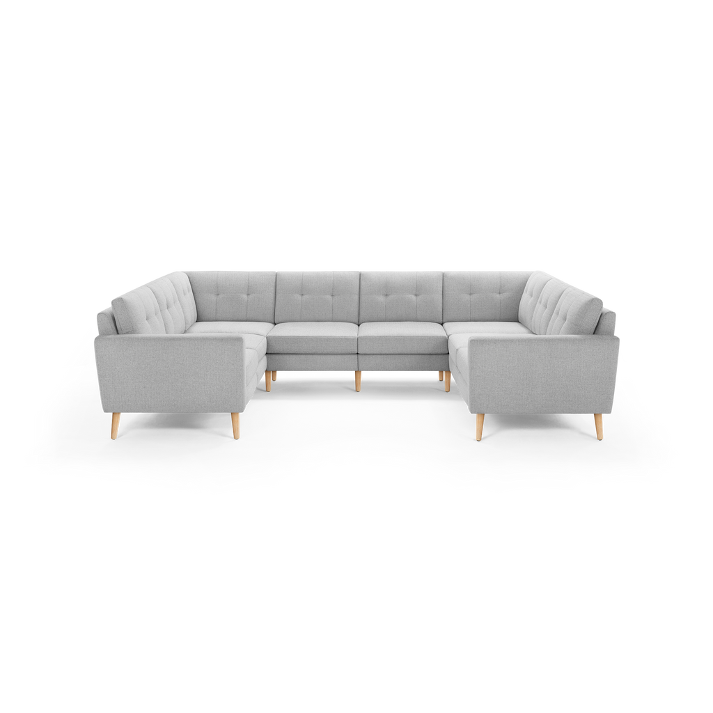 Light gray upholstered U-shaped sectional sofa with tufted back cushions and natural wood tapered legs on black background.