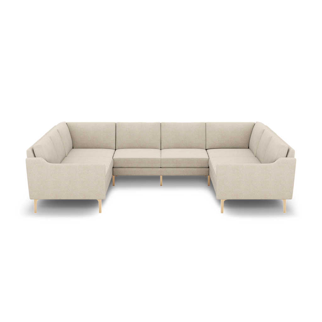 Beige upholstered U-shaped sectional sofa with wooden legs and cushioned seats and backrests, isolated on black background.