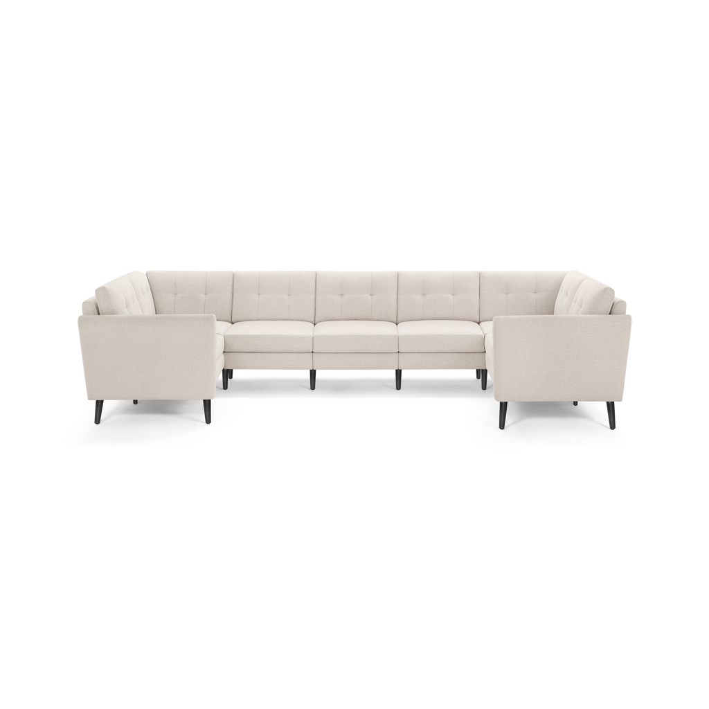 Beige L-shaped sectional sofa with tufted back cushions, slim high black legs, and clean modern design.