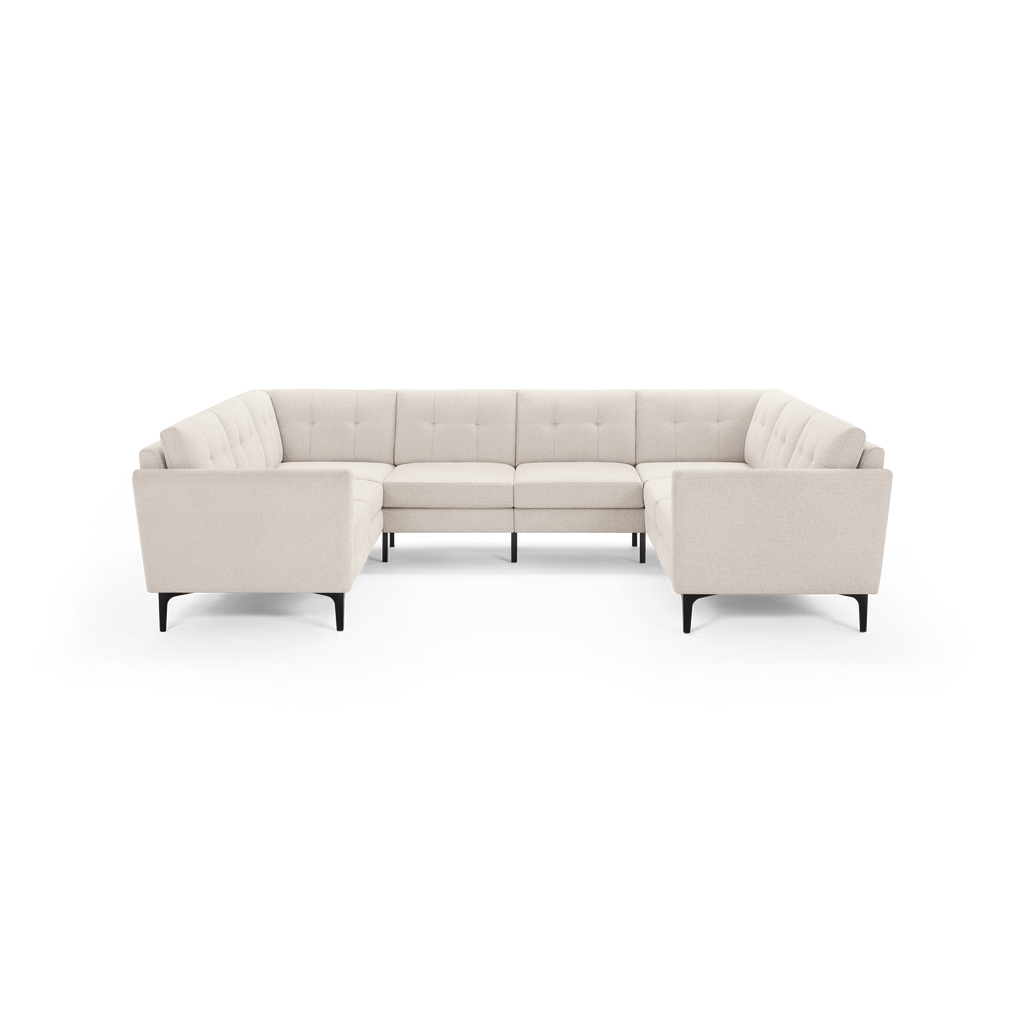 Modern large U-shaped sectional sofa in light beige fabric with tufted back cushions and slim black legs.