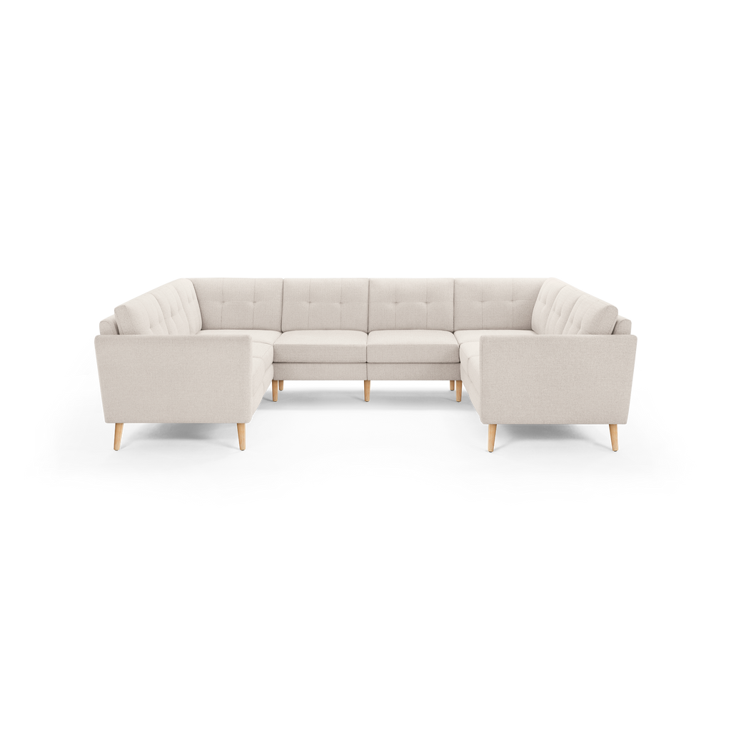 Beige upholstered modular U-shaped sectional sofa with tufted back cushions and light wooden legs, viewed from the front.