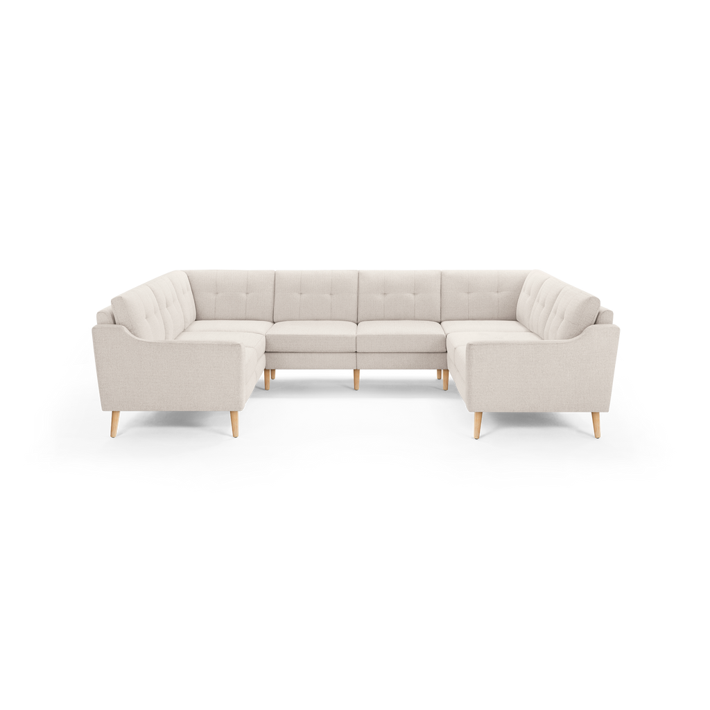 Large U-shaped sectional sofa in light beige fabric with tufted backs and light wooden legs on black background.