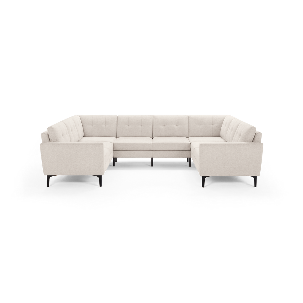 Light beige, modern L-shaped sectional sofa with tufted back cushions and black tapered legs on a transparent background.